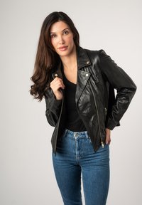 Zwarte leren motorjack met ritssluiting aan de voorkant en zijzakken, gecombineerd met strakke blauwe jeans. Gladde textuur en licht glanzende afwerking.