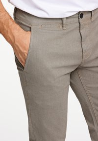 Grijze textuur broek met een aansluitend ontwerp, voorzien van zijzakken en een zichtbare knoopsluiting. Hoogtepunten zijn de contrasterende stiksels.