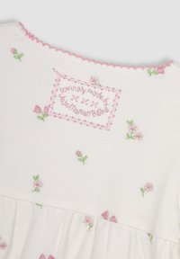 Weißes Baumwollkleid mit zarter rosa Blumenstickerei, gewelltem rosa Ausschnitt und gerafftem Stoff an der Taille für eine weiche Textur.