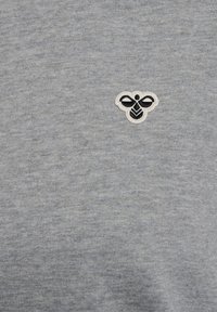 Camicia in cotone grigia con un piccolo logo ricamato a forma di ape bianca e nera sul lato sinistro, che mostra una finitura texturizzata.