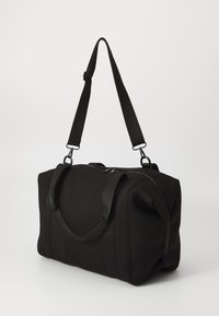 Bolsa de deporte negra hecha de tela texturizada con cierre de cremallera, que cuenta con dos asas de transporte y una correa de hombro ajustable.