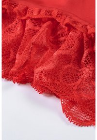 Red lace fabric featuring a frilled edge, intricate patterns, and a soft texture, partially draped over a smooth surface.