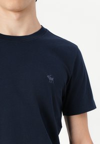 T-shirt di cotone blu navy con colletto alla coreana e maniche corte. Presenta un piccolo logo ricamato di un alce sul petto. Texture liscia.