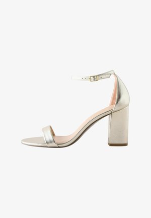 Srebrne metalne sandale na visokom potpetici s blok petom, otvorenom prstima i kaišem oko gležnja koji ima zlatnu kopču, glatke teksture i minimalističkog dizajna.