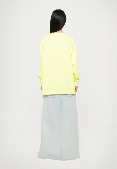 Long-sleeve, bright yellow top paired with a light blue, maxi denim skirt, featuring a straight cut and two back pockets.