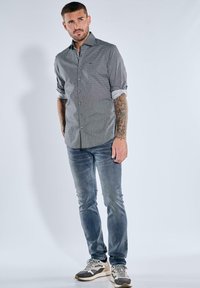 Graues Hemd mit Knopfleiste und kleinem Muster, hochgekrempelte Ärmel, kombiniert mit hellblauen Jeans und grauen Sneakers. Glatter Stoff, figurbetonte Silhouette.
