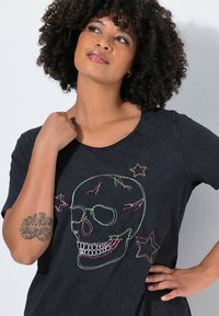 T-shirt noir à manches courtes avec une broderie colorée d'un crâne et d'étoiles. Le tissu semble doux avec une coupe décontractée et un col rond.