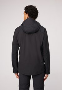 Chaqueta impermeable negra con capucha, que presenta acentos texturizados, un cuello elevado y un logotipo en la parte posterior. Diseñada para uso al aire libre.
