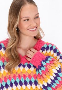 Pulover tricotat multicolor, cu decolteu în V, cu modele îndrăznețe în roz, mov, galben și turcoaz. Mâneci texturate, cu o croială lejeră.