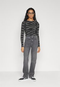 Black and white striped long-sleeve top paired with high-waisted gray denim flared jeans. Model wears black sneakers; background is plain white.