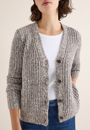 Cardigan grigio texturizzato con apertura frontale, maniche lunghe, quattro grandi bottoni marroni e tasche laterali, indossato sopra una maglietta bianca e jeans blu.