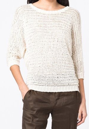 Pull en tricot couleur crème, avec un maillage lâche, un décolleté bateau et des manches trois-quarts. Il présente des poignets et un ourlet côtelés. Porté sur un pantalon marron.