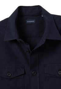 Marineblauw overhemdd met knopen, voorzien van een spitse kraag, twee borstzakken en zwarte knopen. Gemaakt van een textuurstof. Merklabel zichtbaar.