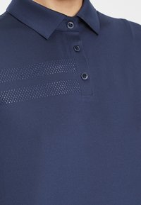 Marinblå polo t-shirt med krage, tre knappar och ett strukturerat randmönster på vänster sida. Slät, lättviktsmaterial.