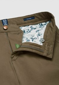Chino broeken van khaki katoenstof, met een ritssluiting, bronzen knoop en een binnenvoering met een patroon in blauw en wit. Etiket met de tekst "M5 CHINO."