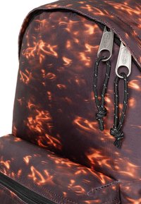 Rucksack aus einem dunklen Stoff mit einem wirbelnden orangefarbenen Flammenmuster, zwei Metallreißverschlüssen und verwobenen schwarzen Kordelzügen.