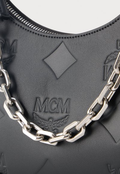 Μαύρη τσάντα από δέρμα με υφή, με ανάγλυφο λογότυπο MCM και διαμάντι μοτίβα, που διαθέτει χοντρή ασημένια αλυσίδα ως χερούλι.