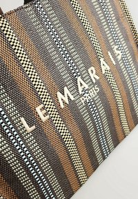 Sac fourre-tout avec des rayures verticales tissées en brun, beige et noir, et "LEMARAIS PARIS" brodé en grandes lettres crème.