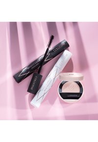 Deux tubes de mascara Collistar Impeccabile noir et blanc avec pinceau, ainsi qu'un boîtier rond ouvert contenant une poudre claire, sur une surface rose.