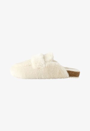 Weicher, cremefarbener, flauschiger Schlupfschuh mit offenem Fersenbereich und flacher Korksohle, seitlich gezeigt.