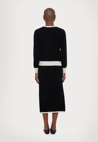 Knit black sweater with a white ribbed hem, matching black long skirt, and black flat shoes, viewed from the back.