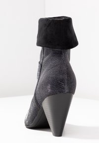 Bottine noire avec un upper texturé et brillant et un revers en suède noir doux ; elle est dotée d'un talon triangulaire pour un supplément de hauteur.