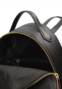 Zaino in pelle nera con cerniera dorata, forma arrotondata e due spallacci. Interno dotato di tasca con cerniera e fodera con marchio. Esterno testurizzato.