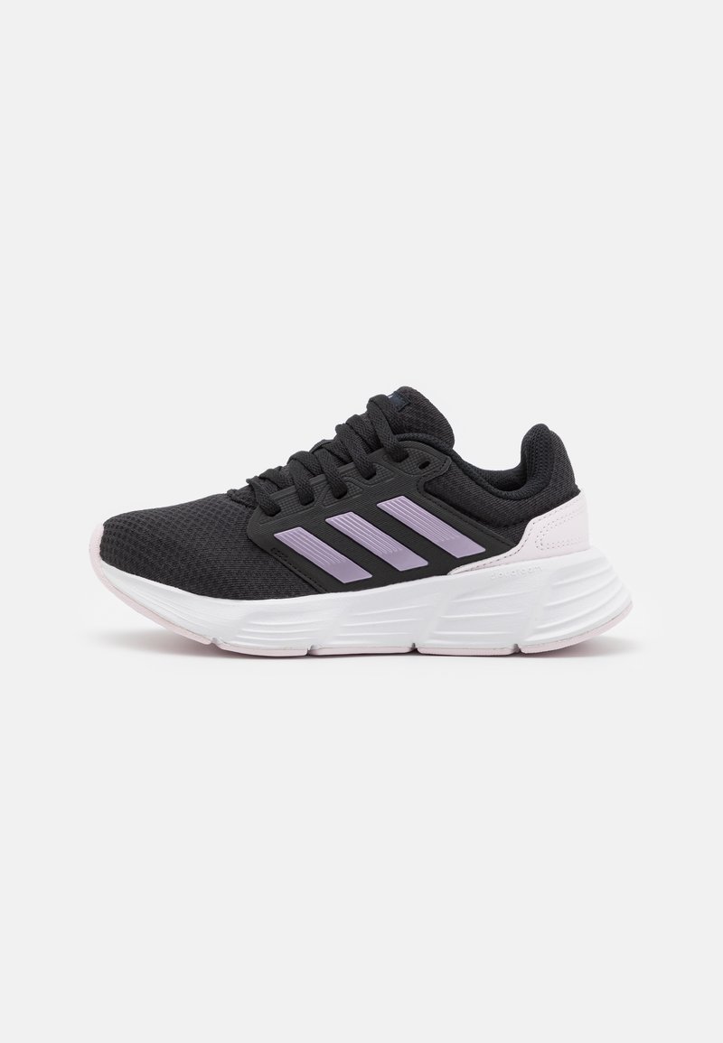 Chaussure de sport noire avec des bandes violet clair, semelle blanche épaisse et lacets noirs, vue de côté sur fond blanc.