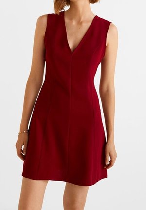 Robe sans manches rouge profond avec col en V, taille ajustée et jupe évasée portée par une personne debout sur un fond blanc.