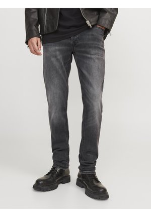 Chaqueta de cuero negra sobre una camisa negra, combinada con jeans oscuros de corte slim y botas negras con cordones y suelas robustas.