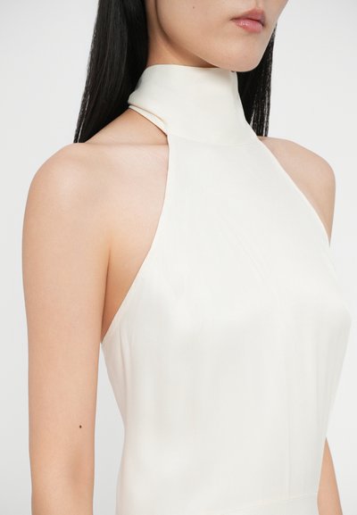Rochie crem fără mâneci, cu guler înalt, având o textură fină și mătăsoasă și un design ajustat, evidențiind umerii și decolteul.