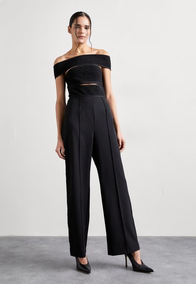 Top scurt negru, cu umerii la vedere, cu o textură subtilă și detalii tăiate, asociat cu pantaloni negri cu talie înaltă și picioare largi, completat cu pantofi cu vârf ascuțit.