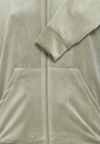 Giacca grigia chiaro morbida con zip, tasche frontali a marsupio e polsini a coste sulle maniche lunghe.