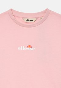 Růžové bavlněné tričko s kulatým výstřihem a bílým logem "ellesse" s oranžovo-červeným polokruhem nad textem na hrudi.