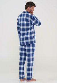 Pijamas de franela a cuadros en azul y blanco que incluyen una camisa de botones y pantalones a juego con una cinturilla elástica. Textura suave.