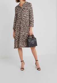 Leopardenmuster Kleid mit V-Ausschnitt, drei Viertelärmel und gestuftem Saum. Kombiniert mit einer schwarzen Handtasche mit rundem Griff und Akzenten.