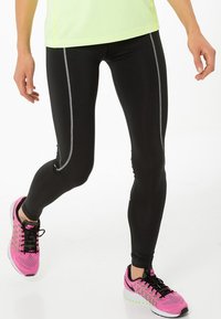 Leggings negros con costuras laterales reflectantes, hechos de material elástico. Combinados con zapatillas deportivas rosas con cordones negros y diseño texturizado.
