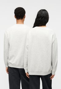 Γκρι φούτερ με χαμηλωμένους ώμους, ριμπ μανσέτες και τελείωμα. Μαλακή υφή, απλός σχεδιασμός, φορεμένο με σκουρόχρωμο τζιν. Πλάγια όψη δύο φιγούρων.