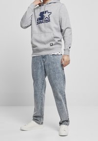 Grijs hoodie sweatshirt met een marineblauw "Starter" logo en een voorzak, gedragen met lichtblauwe denim jeans en witte sneakers.
