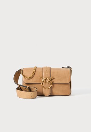 Beige Wildleder-Handtasche mit einer goldfarbenen Vogelmotiv-Schnalle, einem abnehmbaren Kettenriemen und einem glatten Leder-Schulterriemen.