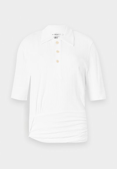 Polo blanc à manches courtes en tissu côtelé texturé, avec un col pointu et trois boutons dorés à l'avant.