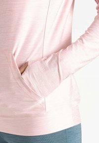 Helles rosa Langarmoberteil mit Kängurutasche. Der Stoff hat eine dezente Textur. Verfügt über Daumenlöcher an den Bündchen und ein kleines Logodetail.