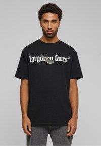 Sort bomulds t-shirt med teksten "glemte ansigtter" i hvid og et fjer grafik. Klassisk crew neck og korte ærmer.