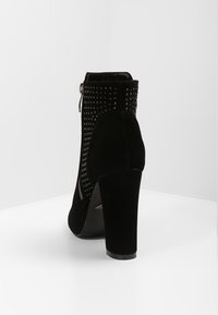 Černá semišová kotníková bota na vysokém podpatku, s cvočky po celé délce zadního zipu pro přidanou texturu a design.