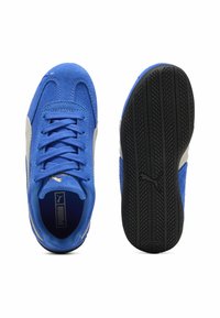 Zapatillas de ante azul con acentos grises, suelas de goma negra planas, cordones texturizados y un logo dorado en el lateral. Vista desde arriba.