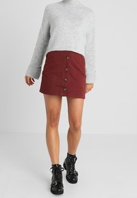 Grå kortärmad tröja, vinröd kjol med knappar framtill, svarta snörstövlar. Kjolen har fem knappar; tröjan har ribbade ärmslut.