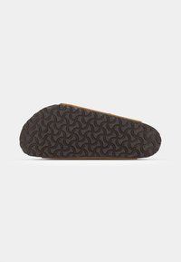 Sola de calçado com uma base de borracha texturizada castanha, apresentando um padrão de ondas, afinando na parte da frente para suporte ergonómico.