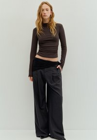 Braunes, langärmliges, figurbetontes Oberteil kombiniert mit weit geschnittenen, dunkel gestreiften Hosen mit gerafftem schwarzem Bund und weicher Stoffstruktur.