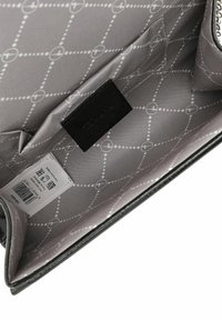 Wnętrze torby na ramię z szarym tekstylnym wykończeniem w geometryczny wzór, czarną skórzaną metką oraz widoczną etykietą z kodem kreskowym.