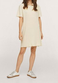 Vestido polo color crema con mangas cortas, un dobladillo ondulado y una textura ligera. Combinado con zapatillas blancas con detalles grises.